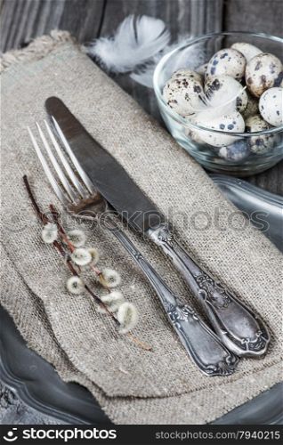 Vintage cutlery on rough napkin, willow twigs and quail eggs in a glass bowl