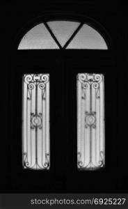 Vintage door frame with decorative motif and arched glass lite. Abandoned neoclassical house dark interior black and white.