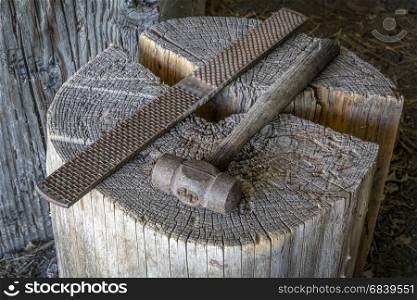 vintage file and hammer against wooden log in an old blacksmith or farm workshop