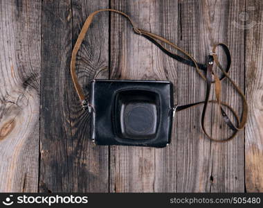 Vintage film camera in a leather case on a wooden gray background, top view