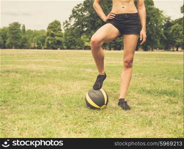 Vintage filtered shot of a fit and athletic young woman is standing on the grass in a park with a medicine ball