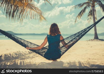 Vintage filtered shot of a young woman sitting in a hammock on a tropical beach