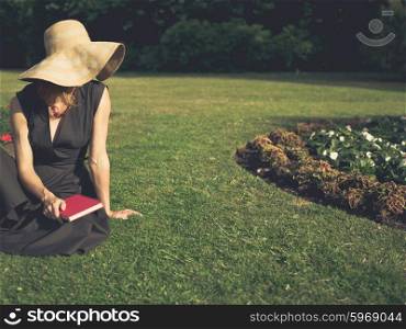 Vintage filtered shot of an elegant woman sitting on the grass in a park with a book