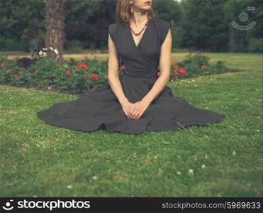 Vintage filtered shot of an elegant woman sitting on the grass in a park by a flowerbed