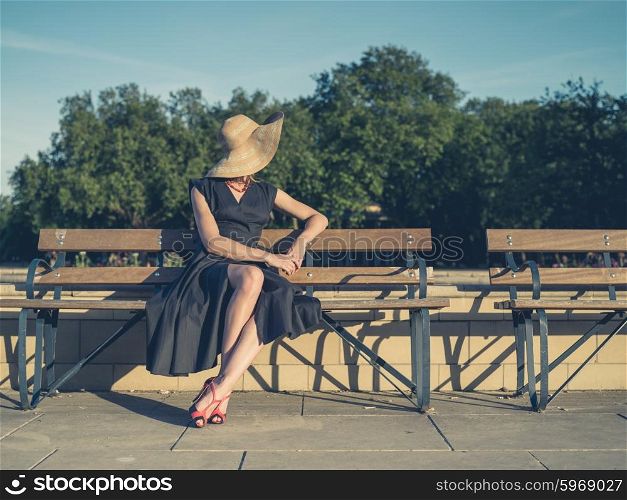Vintage filtered shot of an elegant young woman in dress and high heels sitting on a park bench