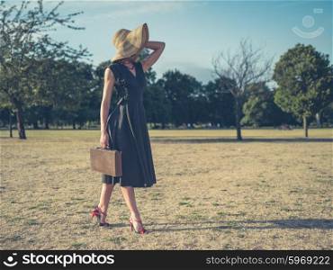 Vintage filtered shot of an elegant young woman in high heels and a dress walking in the park with a briefcase