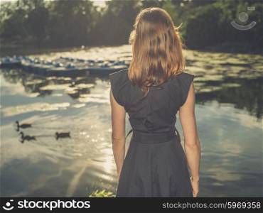 Vintage filtered shot of an elegant young woman standing by a lake in a park at sunset