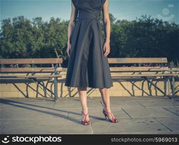Vintage filtered shot of an elegant young woman wearing a dress and standing by some park benches