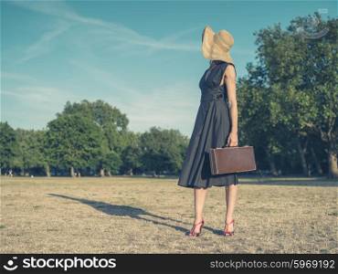 Vintage filtered shot of an elegant young woman wearing a dress and a hat standing in the park with a briefcase