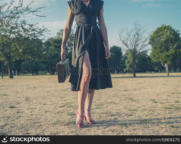 Vintage filtered shot of an elegant young woman wearing a dress and high heels standing in a park with a briefcase
