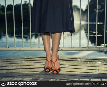 Vintage filtered shot of the legs and feet of an elegant woman standing on a pier by a lake in a park