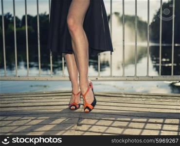 Vintage filtered shot of the legs and feet of an elegant woman standing on a pier by a lake in a park