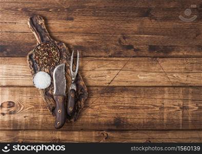 Vintage fork and knife for meat on wooden chopping board with salt and pepper on wooden background.