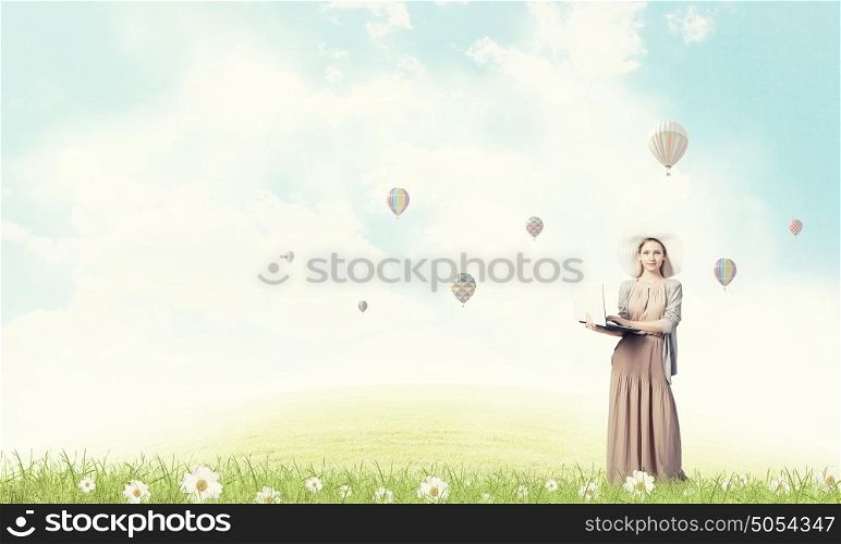 Vintage girl with laptop. Young elegant gil in hat and long dress using laptop