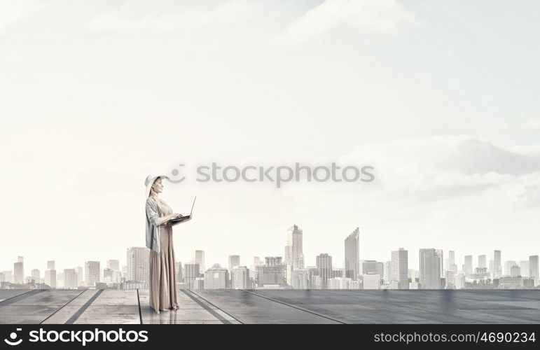 Vintage girl with laptop. Young lady in hat and long dress using laptop