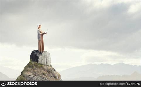 Vintage girl with laptop. Young lady standing on rock top using laptop