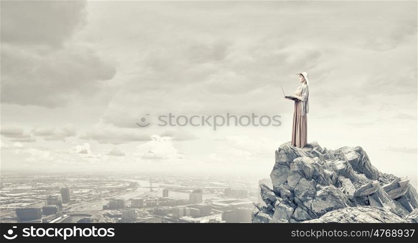 Vintage girl with laptop. Young lady standing on rock top using laptop