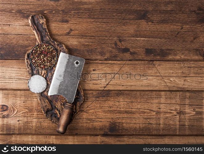 Vintage hatchet for meat on wooden chopping board with salt and pepper on wooden background.