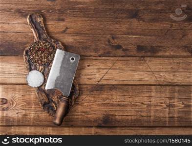 Vintage hatchet for meat on wooden chopping board with salt and pepper on wooden background.