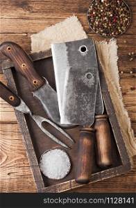 Vintage hatchets for meat in wooden box with salt and pepper on wooden background with linen towel and fork and knife.