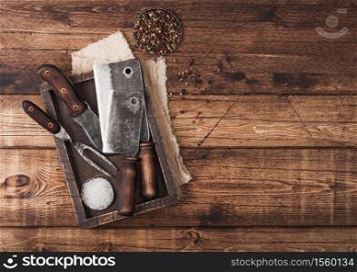 Vintage hatchets for meat in wooden box with salt and pepper on wooden background with linen towel and fork and knife. Space for text