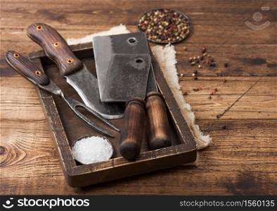 Vintage hatchets for meat in wooden box with salt and pepper on wooden background with linen towel and fork and knife. Top view