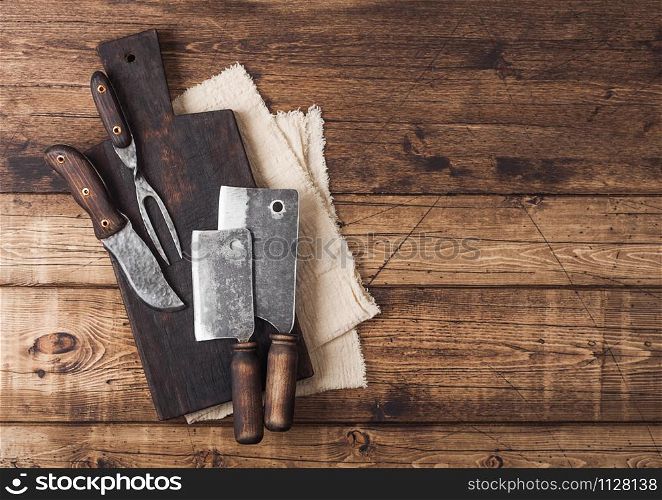 Vintage hatchets for meat on wooden chopping board on wooden table background with linen towel and fork and knife. Space for text