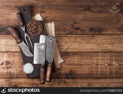 Vintage hatchets for meat on wooden chopping board with salt and pepper on wooden table background with linen towel and fork and knife. Space for text