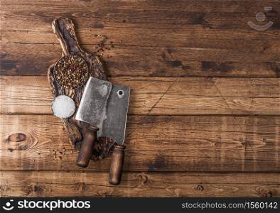 Vintage hatchets for meat on wooden chopping board with salt and pepper on wooden background.