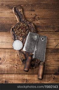 Vintage hatchets for meat on wooden chopping board with salt and pepper on wooden background.