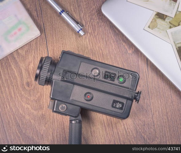 Vintage image with old black Video camera 8mm,old photo,laptop,pen and passport on wood table.