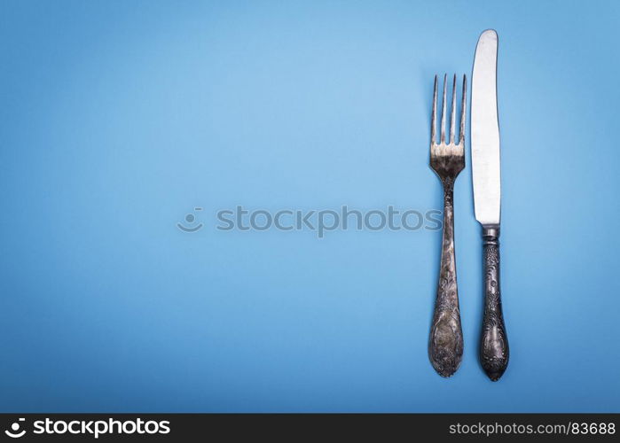 vintage iron fork and knife on a blue background, empty space on the left, top view