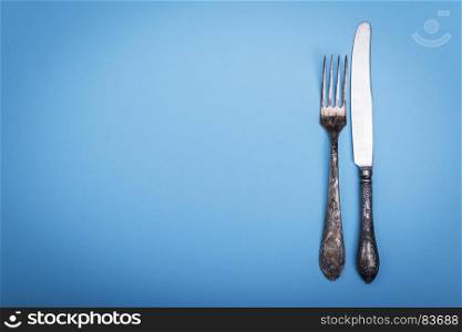 vintage iron fork and knife on a blue background, empty space on the left, top view