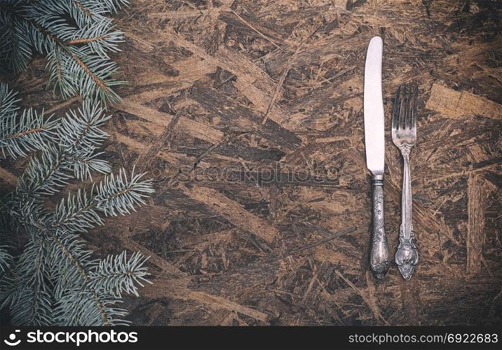 vintage iron fork and knife on a brown wooden background, empty space in the middle, side view green spruce branch