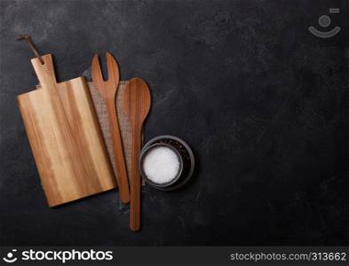 Vintage kitchen wooden utensils with chopping board on black stone table background. Top view. Space for text.