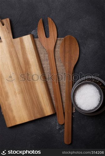 Vintage kitchen wooden utensils with chopping board on black stone table background. Top view.