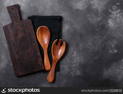 Vintage kitchen wooden utensils with chopping board on black stone table background. Top view. Space for text.