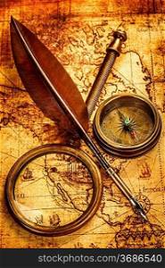 Vintage magnifying glass, compass and goose quill pen lying on an old map.
