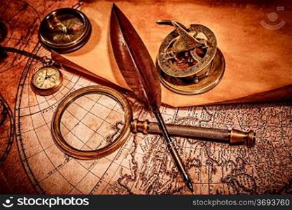 Vintage magnifying glass, compass, goose quill pen and a pocket watch lying on an old map.