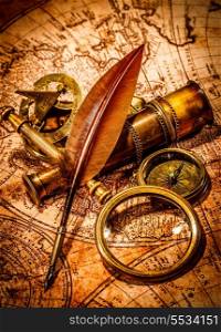 Vintage magnifying glass, compass, goose quill pen and spyglass lying on an old map.