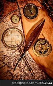 Vintage magnifying glass, compass, goose quill pen, spyglass and a pocket watch lying on an old map.