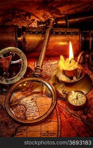 Vintage magnifying glass, compass, pocket watch, spyglass lie on an old ancient map with a lit candle