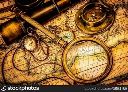 Vintage magnifying glass, compass, telescope and a pocket watch lying on an old map.