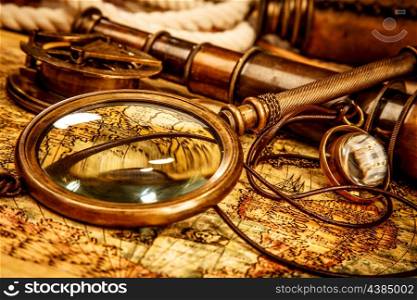 Vintage magnifying glass, compass, telescope and a pocket watch lying on an old map.