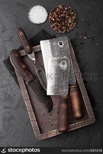 Vintage meat knife and fork and hatchet in old wooden box on black table background. Butcher utensils.