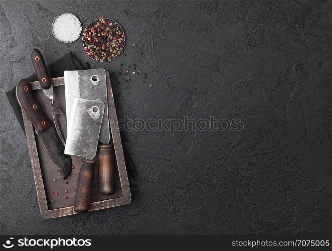 Vintage meat knife and fork and hatchet in old wooden box on black table background. Butcher utensils.