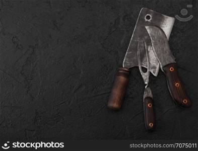 Vintage meat knife and fork and hatchet on black table background. Butcher utensils.