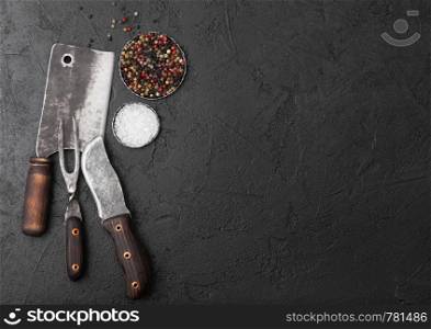 Vintage meat knife and fork and hatchet on black table background. Butcher utensils. Salt and pepper