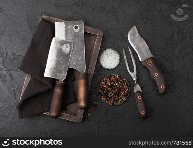 Vintage meat knife and fork and hatchets with vintage chopping board and black table background. Butcher utensils.