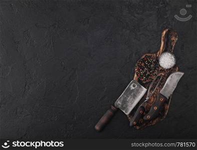 Vintage meat knife and fork on vintage chopping board and black stone table background. Butcher utensils.